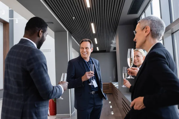 Multiethnic business colleagues holding champagne glasses during conversation on symposium — Stock Photo