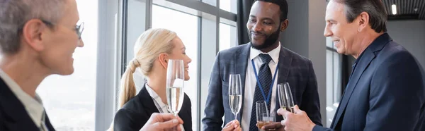 Multiethnische Geschäftsleute halten Champagnergläser während der Diskussion über Konferenz, Banner — Stockfoto