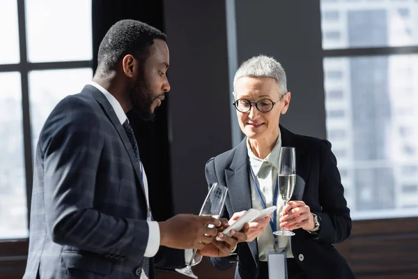 Interracial business partners looking at mobile phones while talking during conference — Stock Photo