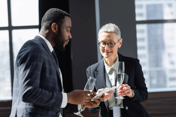 Socios comerciales interracial mirando a los teléfonos móviles mientras habla durante la conferencia - foto de stock