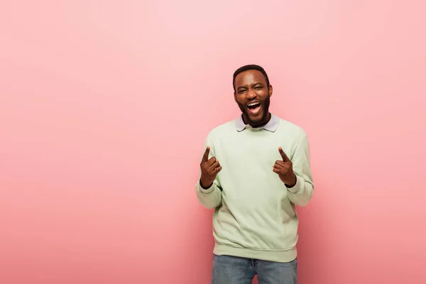 Positive african american man pointing with fingers on pink background — Stock Photo