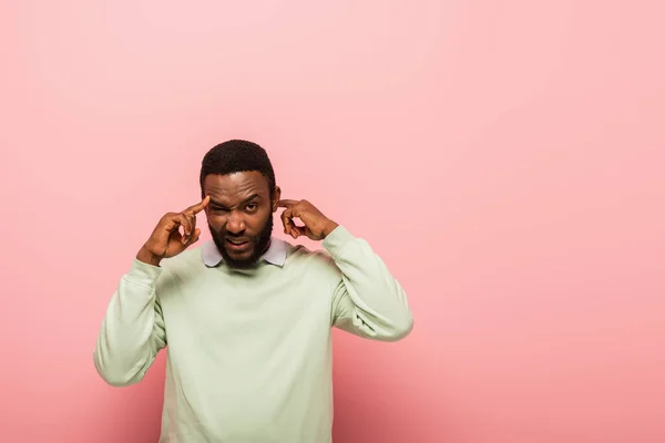 Confused african american man pointing at head on pink background — Stock Photo