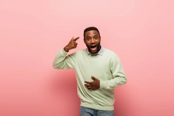 Emocionado hombre afroamericano apuntando a la cabeza sobre fondo rosa - foto de stock