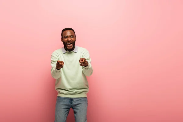 Allegro uomo africano americano che punta con le dita alla fotocamera su sfondo rosa — Foto stock