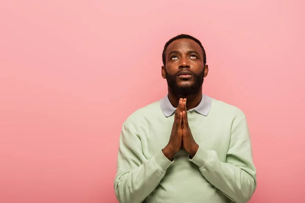 Uomo afroamericano con le mani in preghiera guardando in alto isolato su rosa — Foto stock