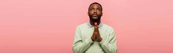 Uomo afroamericano con le mani in preghiera guardando in alto isolato sul rosa, striscione — Foto stock