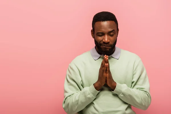 African american man standing with praying hands isolated on pink — Stock Photo