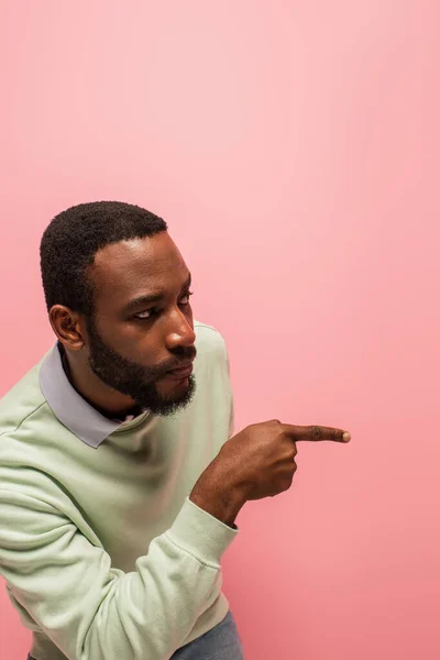 Uomo afroamericano in maglione che punta con il dito lontano isolato su rosa — Foto stock