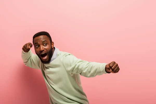 Screaming african american man with hands in fists on pink background — Stock Photo