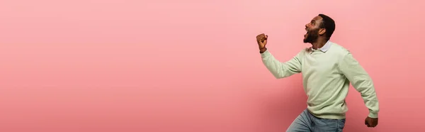 Вид сбоку изумленного африканского мужчины, показывающего жест Фабрегаса на розовом фоне, баннер — стоковое фото