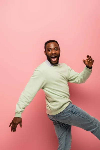 Cheerful african american man looking at camera while walking on pink background — Stock Photo