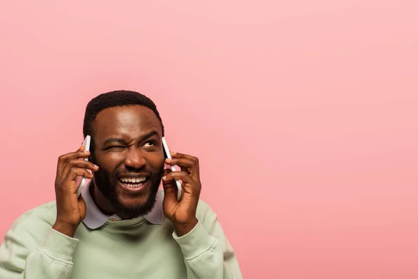 Африканський американець, який підморгує, розмовляючи на смартфонах, ізольованих рожевим. — стокове фото