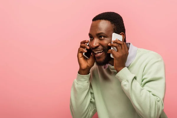 Joven afroamericano hablando en teléfonos móviles aislados en rosa - foto de stock