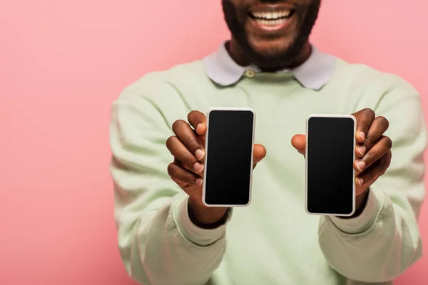Vista cortada de smartphones com tela em branco em mãos de homem americano africano sorridente isolado em rosa — Fotografia de Stock