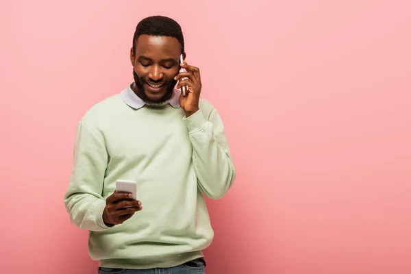 Молодий афроамериканець розмовляє і користується мобільним телефоном на рожевому фоні. — стокове фото