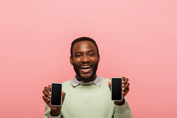 Fröhlicher afrikanisch-amerikanischer Mann mit Handys isoliert auf rosa — Stockfoto