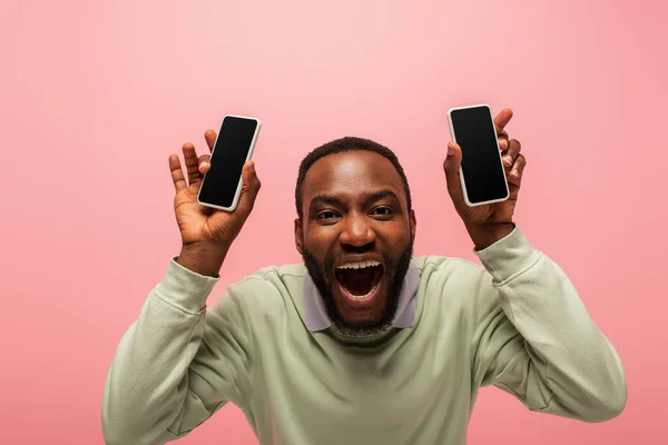 Aufgeregter afrikanisch-amerikanischer Mann mit Mobiltelefonen blickt isoliert in die Kamera auf rosa — Stockfoto