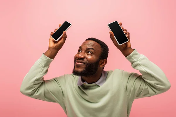 Smartphones en manos del hombre afroamericano sonriente aislado en rosa - foto de stock
