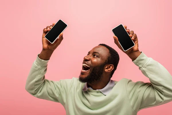 Hombre afroamericano feliz mirando el teléfono inteligente con pantalla en blanco aislado en rosa - foto de stock