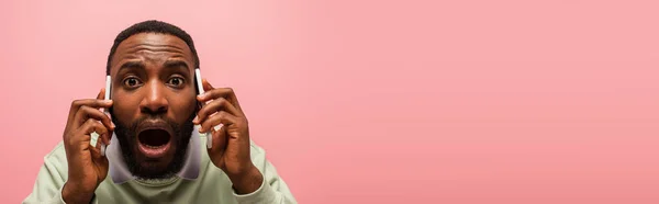 Приголомшений афроамериканець розмовляє на смартфонах ізольованих рожевим, з копіювальним простором, банером. — стокове фото