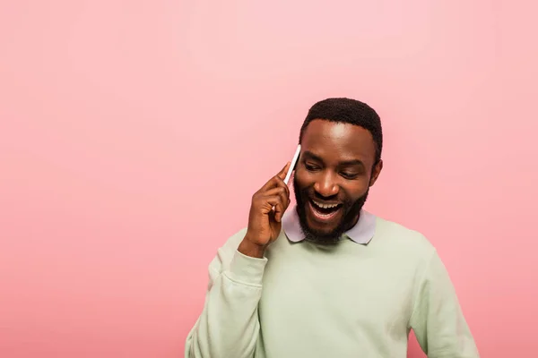 Усміхнений афроамериканець розмовляє по мобільному телефону ізольованим рожевим. — стокове фото