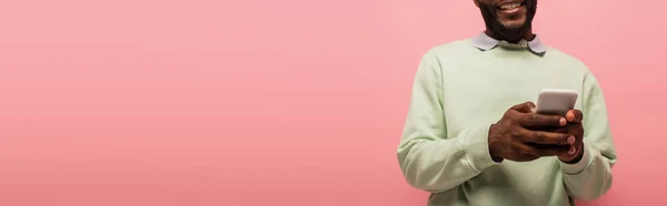 Vue recadrée de l'homme afro-américain sur fond flou à l'aide d'un smartphone isolé sur rose, bannière — Photo de stock