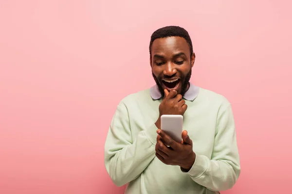 Homem afro-americano positivo usando celular isolado em rosa — Fotografia de Stock