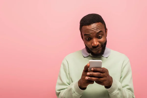 Hombre afroamericano mensajes de texto en el teléfono inteligente aislado en rosa - foto de stock