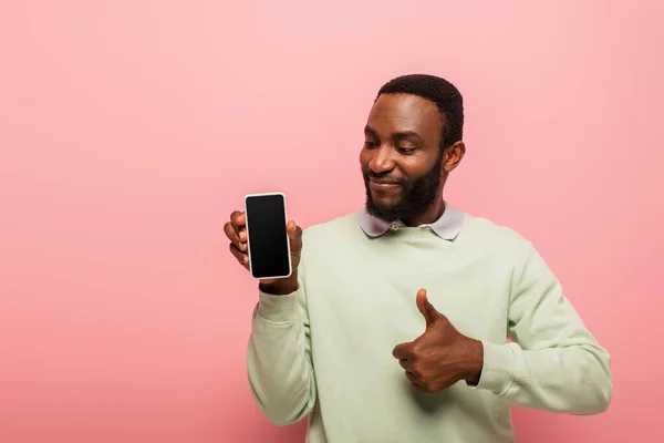 Sorrindo afro-americano homem segurando smartphone e mostrando como gesto isolado em rosa — Fotografia de Stock