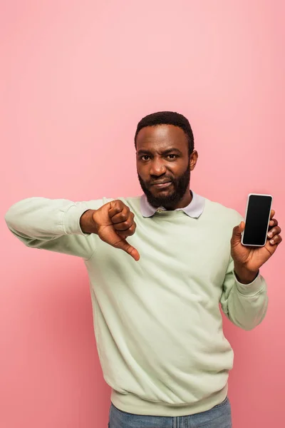 Скептически настроенный афроамериканец демонстрирует неприязнь к смартфону на розовом фоне — стоковое фото