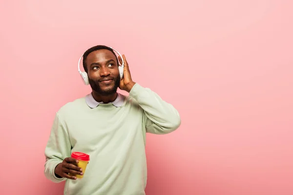 Africain américain dans un casque tenant tasse en papier sur fond rose — Photo de stock