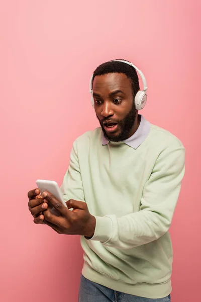 Homem americano africano excitado em fones de ouvido usando smartphone isolado em rosa — Fotografia de Stock