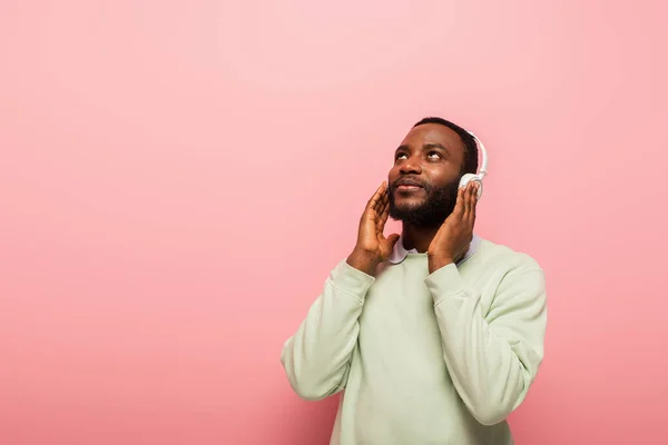 Молодий афроамериканець слухає музику в навушниках на рожевому фоні. — стокове фото