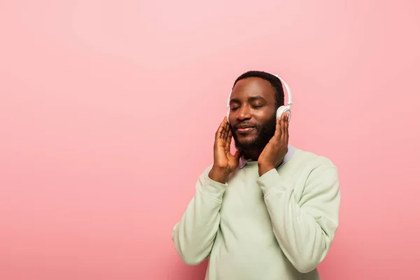 Африканский американец в наушниках слушает музыку с закрытыми глазами на розовом фоне — стоковое фото