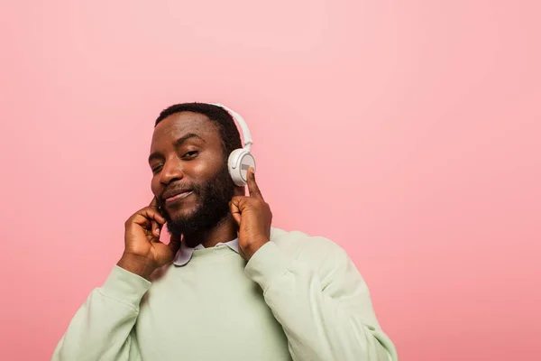Sonriente hombre afroamericano en auriculares mirando la cámara aislada en rosa - foto de stock