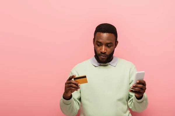 African american man using credit card and smartphone during online shopping on pink background — Stock Photo