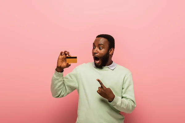 Excited african american man pointing at credit card on pink background — Stock Photo