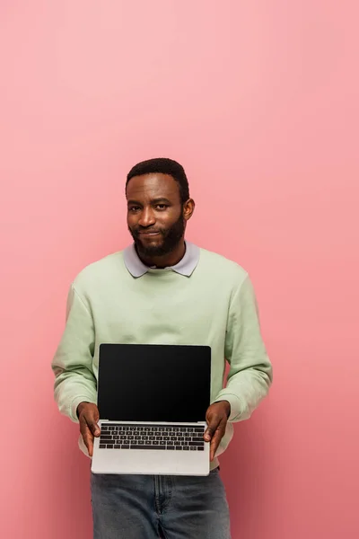 Découragé homme afro-américain montrant ordinateur portable avec écran blanc sur fond rose — Photo de stock