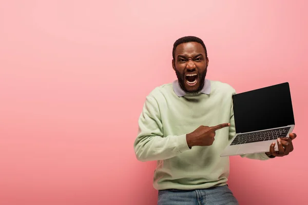 Aufgeregter afrikanisch-amerikanischer Mann zeigt auf Laptop mit leerem Bildschirm auf rosa Hintergrund — Stockfoto