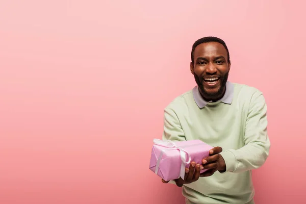 Homem americano africano alegre mostrando presente isolado no rosa — Fotografia de Stock