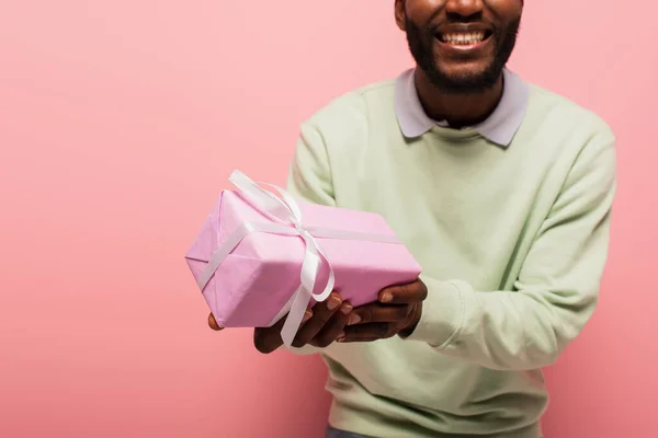 Partial view of smiling african american man holding gift box isolated on pink — Stock Photo