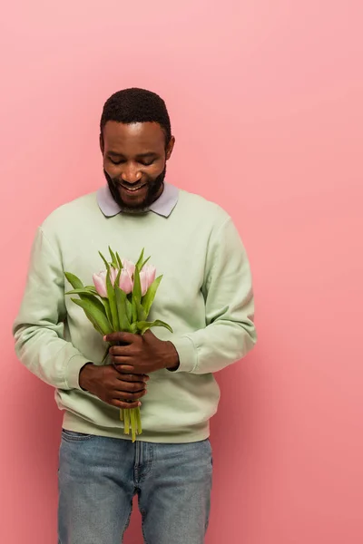 Felice uomo africano americano che tiene bouquet di tulipani su sfondo rosa — Foto stock