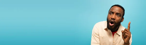 Astonished african american man pointing up with fingers isolated on blue, banner — Stock Photo