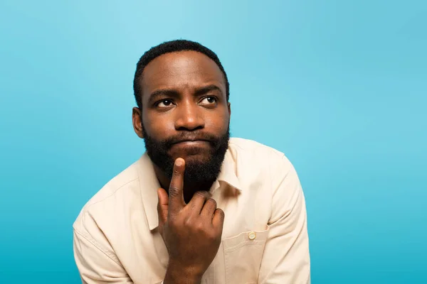 Pensoso afro americano uomo toccare faccia mentre guardando lontano isolato su blu — Foto stock