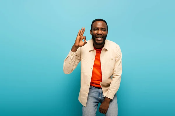 Laughing african american man showing okay sign while looking at camera on blue background — Stock Photo