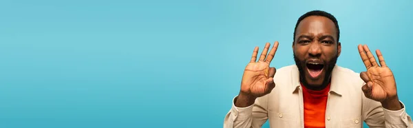 Aufgeregter afrikanisch-amerikanischer Mann zeigt Okay-Zeichen isoliert auf blauem Banner — Stockfoto