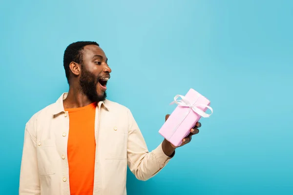 Amazed african american man holding present isolated on blue — Stock Photo