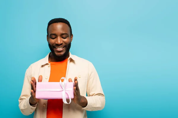 Pleased african american man holding gift box isolated on blue — Stock Photo