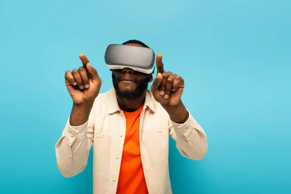 Afrikanisch-amerikanischer Mann in vr Headset zeigt mit den Fingern, während Gaming isoliert auf blau — Stockfoto