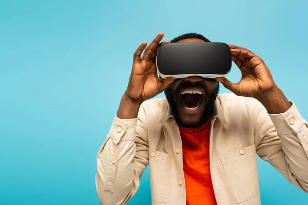 Emocionado afro-americano homem ajustando vr headset enquanto jogos isolados em azul — Fotografia de Stock